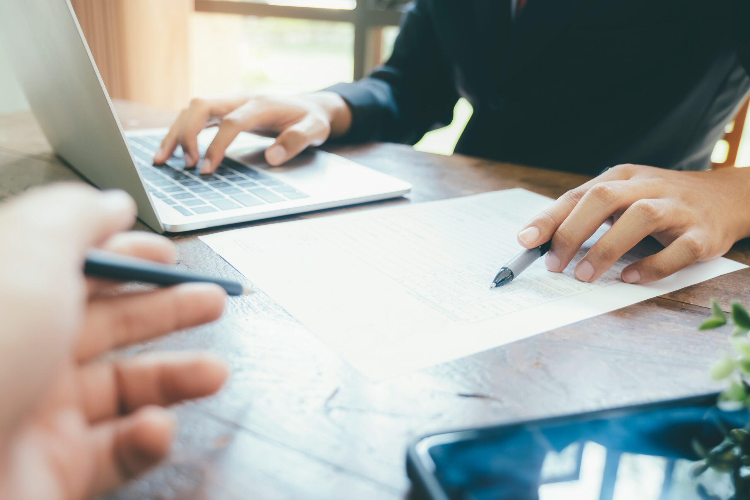 A professional in a suit working on a laptop and reviewing paperwork at a desk, representing HR outsourcing for professional services.